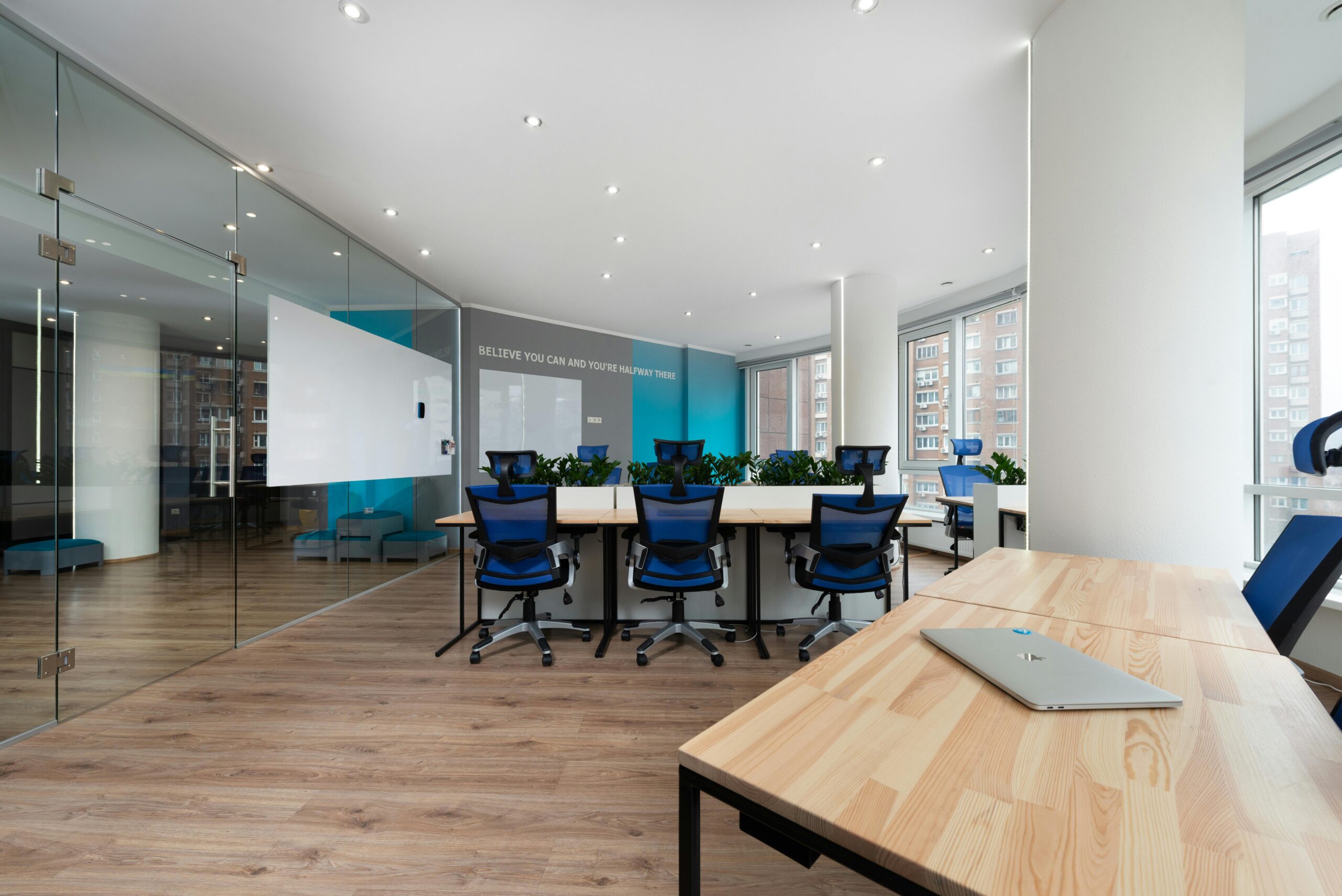 Blue armchairs at table near green plants placed in light boardroom with modern laptop and window in stylish office building